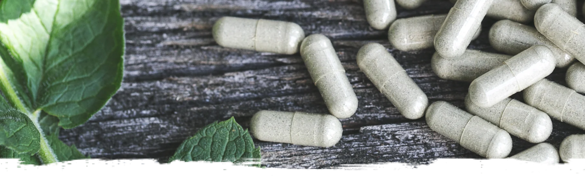 Green supplement tablets placed on a wooden surface, a leaf placed on the left.